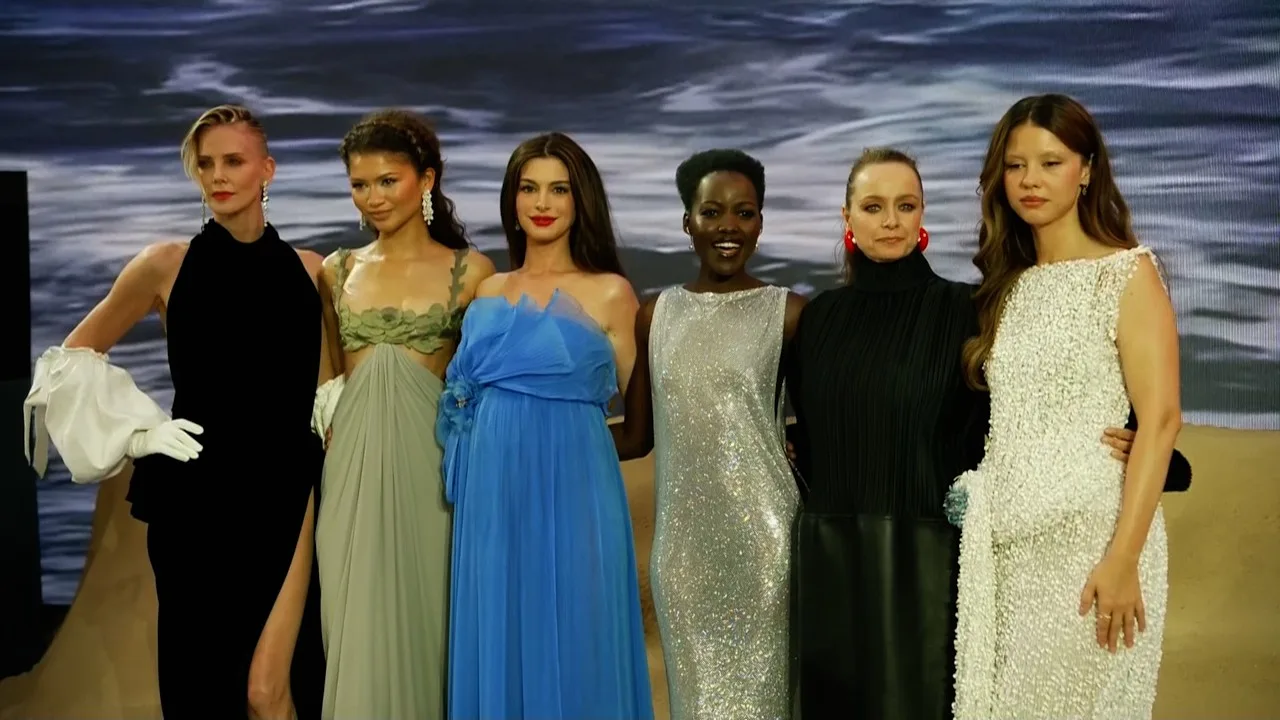 Charlize Theron in a black gown and white opera gloves with The Odyssey cast at the London premiere